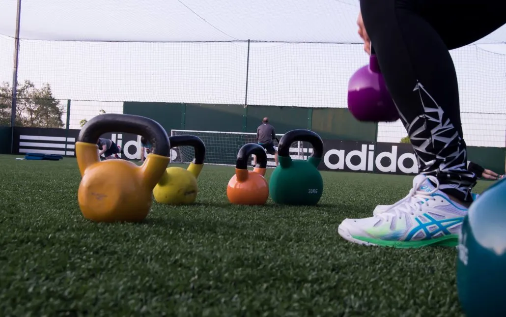 Kettle bell training outdoors during a circuits class. Lady doing kettle bell swings in focus of screen